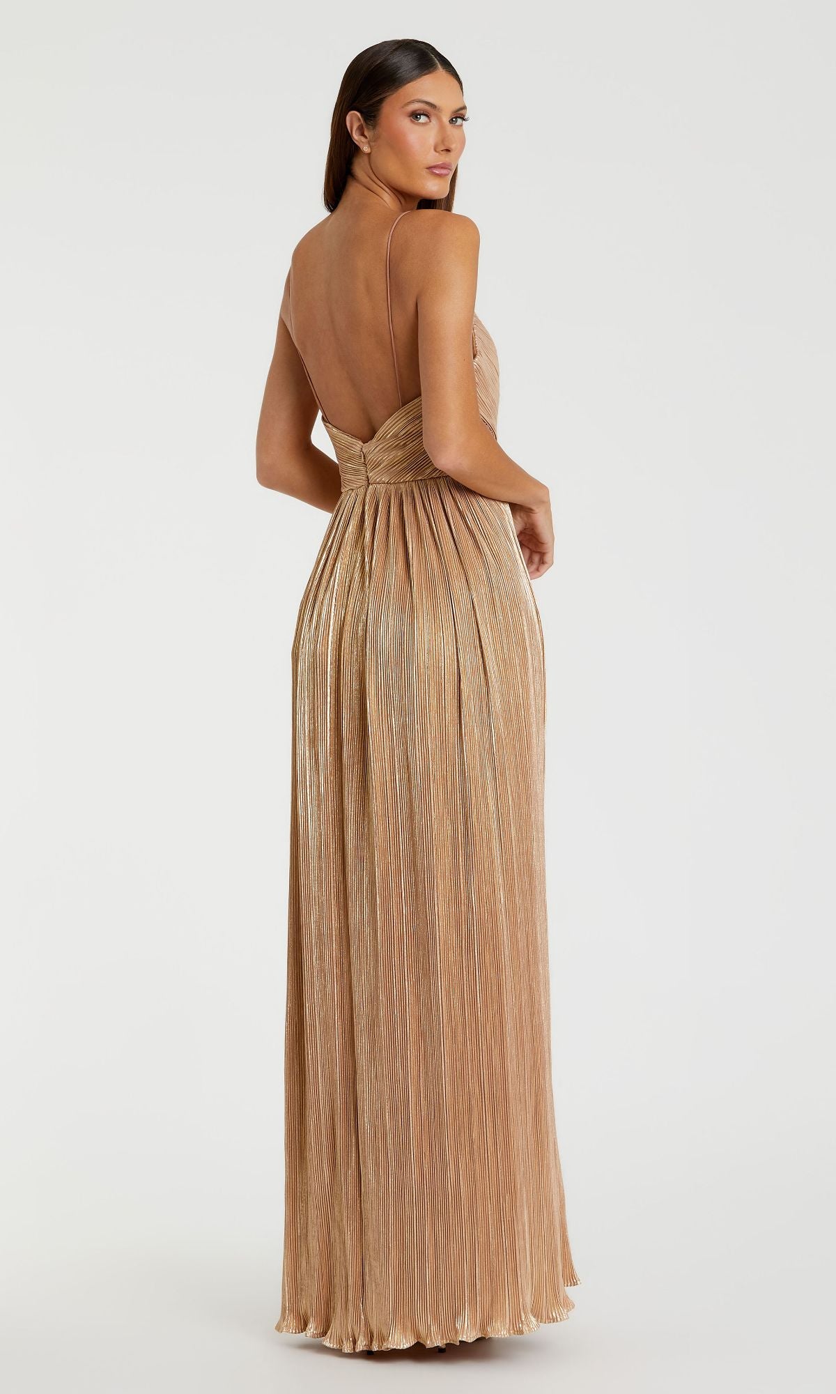 A woman stands looking over her shoulder in the Mac Duggal 26275 Long Gold Pleated Formal Dress, featuring thin straps, an open back, and a metallic finish.